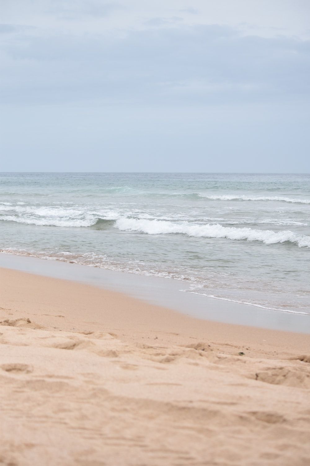  Meer Strand Hintergrundbild 1000x1500. Foto zum Thema Eine Person, die an einem Strand spazieren geht und ein Surfbrett trägt