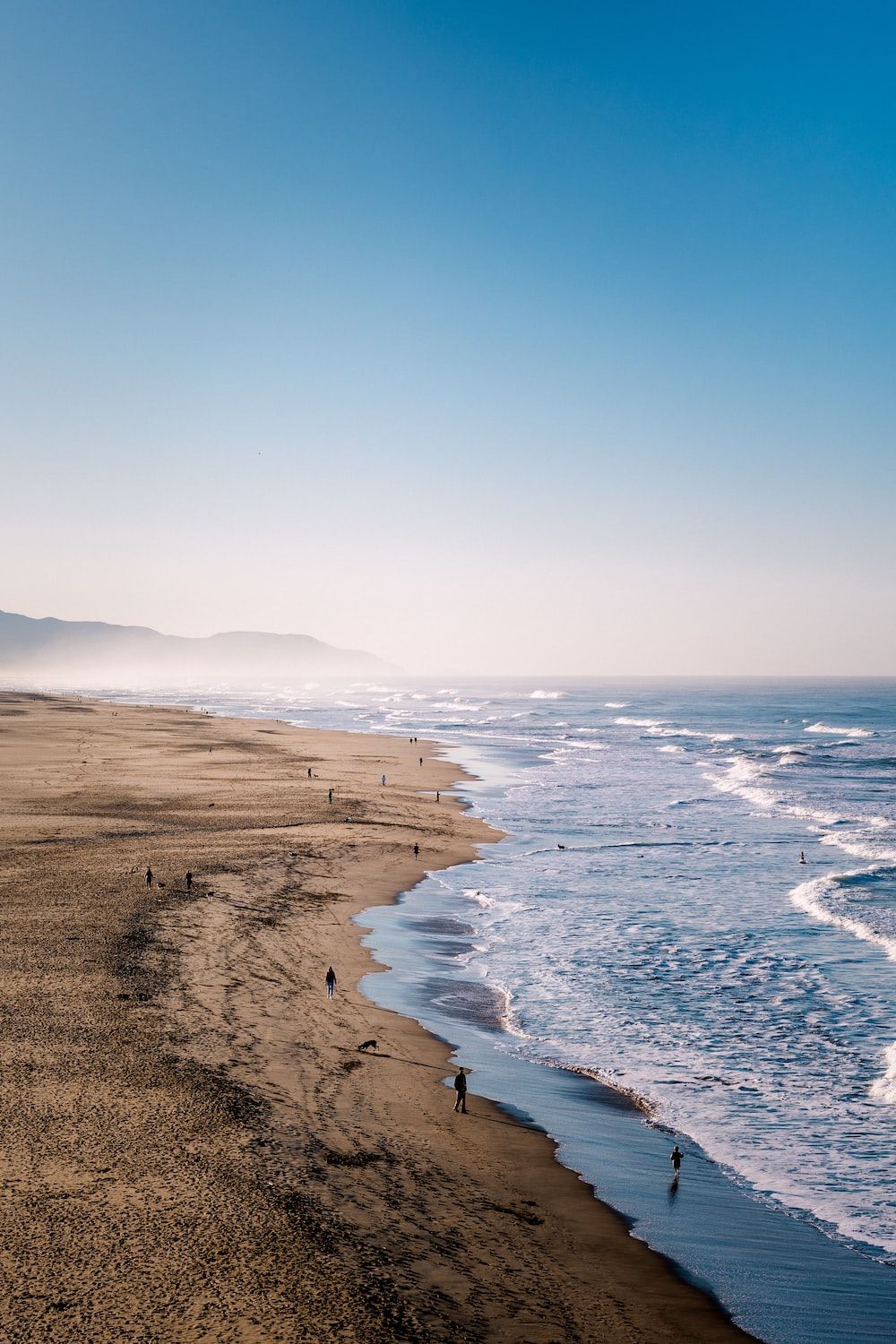  Meer Strand Hintergrundbild 1000x1500. Foto zum Thema Eine Gruppe von Menschen, die an einem Strand am Meer entlang spazieren gehen