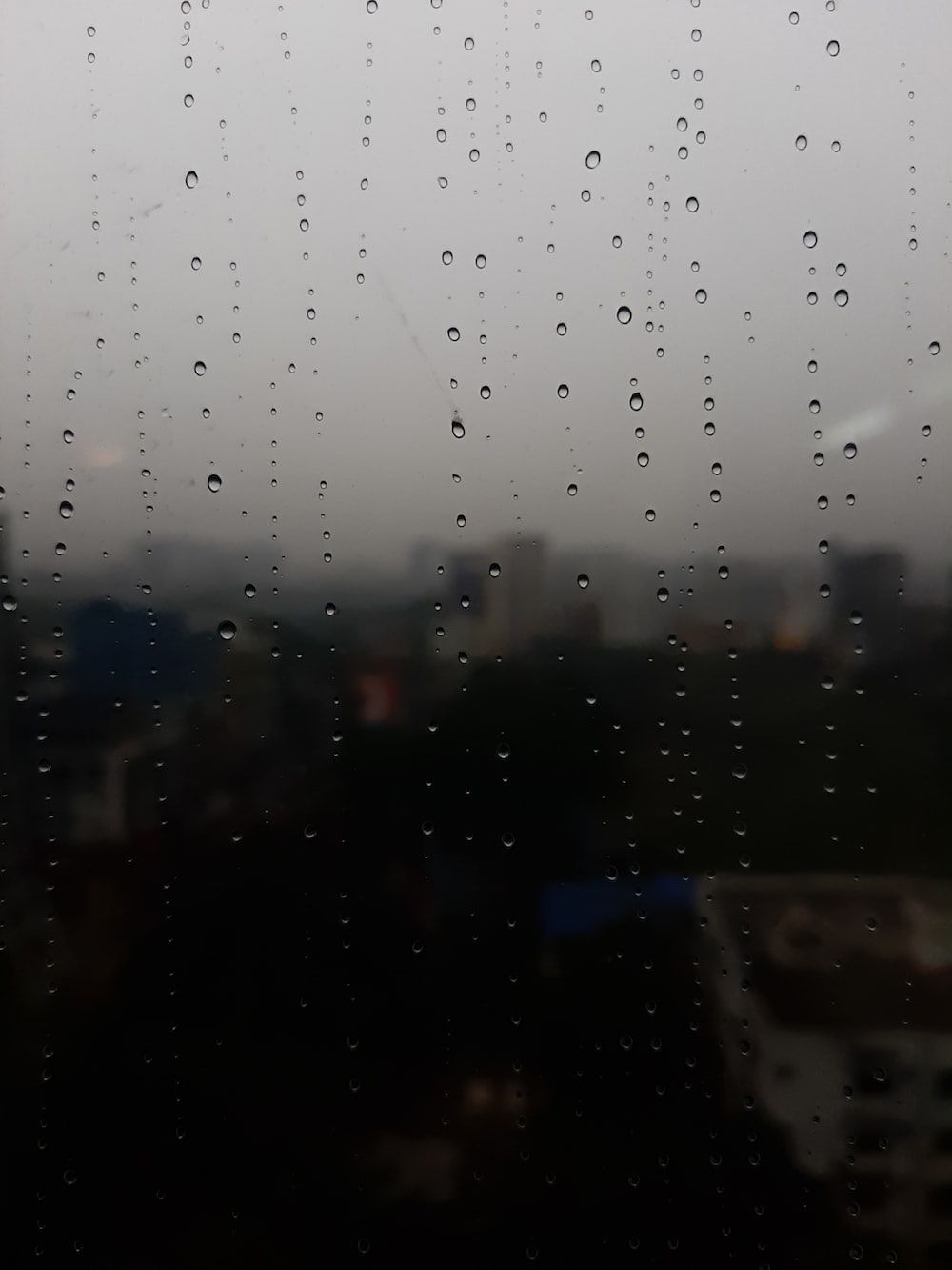  Regen Hintergrundbild 1000x1333. Foto zum Thema Regentropfen auf ein Fenster mit einer Stadt im Hintergrund